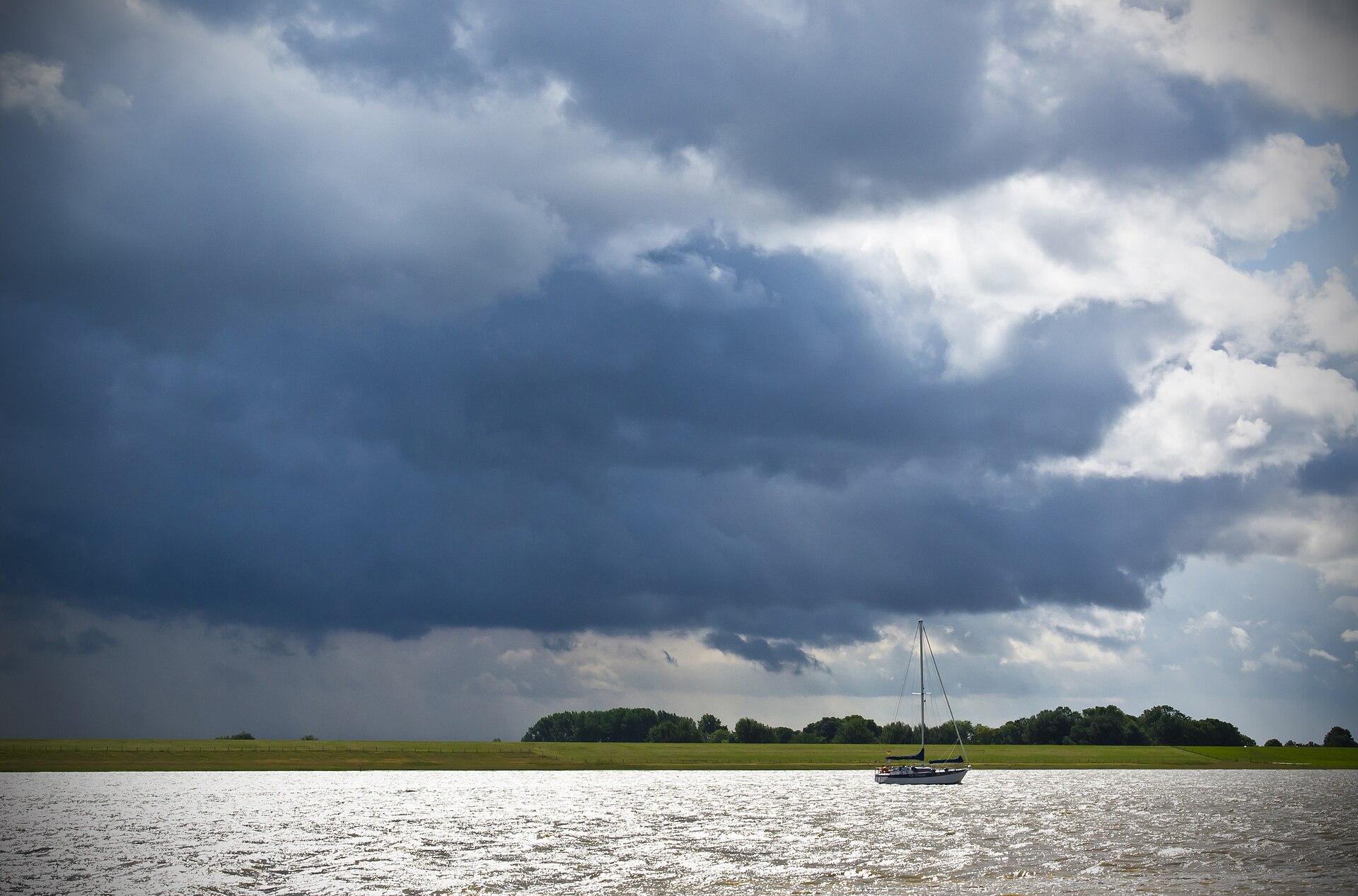 A small sailboat anchored under a dark, threatening storm cloud on open water